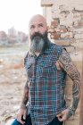 Татуйований зрілий чоловік хіпстер спирається на стіну зруйнованої будівлі — стокове фото