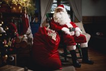 Retrato de Papai Noel sentado em cadeira com saco de presentes — Fotografia de Stock