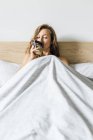 Mujer joven bebiendo café en la cama - foto de stock