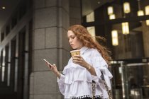 Giovane donna con caffè da asporto guardando smartphone sul marciapiede, New York, Stati Uniti — Foto stock