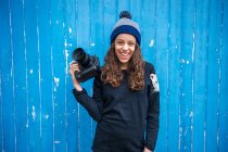 Mädchen hält Kamera vor blauem Holzpaneel-Hintergrund — Stockfoto