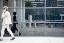 Young man walking past office building and using smartphone — Stock Photo