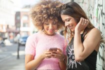 Две молодые женщины на улице, смотрят на смартфон — стоковое фото