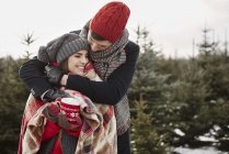 Romántica pareja joven en el bosque de árboles de Navidad envuelta en manta - foto de stock