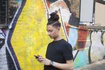 Вид збоку Молодий чоловік використовує смартфон проти стіни з графіті — стокове фото