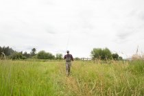 Fischer mit Angelrute, der auf dem Grasfeld geht, Klare Gabel, Montana — Stockfoto