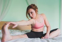 Young woman stretching and training on bed — Stock Photo