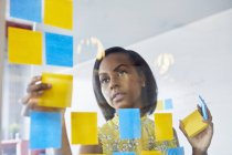 Young woman in office sticking notes to glass in office — Stock Photo