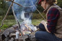Woman sitting beside camp fire and cooking food, Colgate Lake Wild Forest, Catskill Park, New York State, USA — Stock Photo