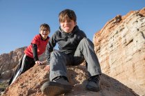 Портрет мальчиков, сидящих на скале, смотрящих в камеру, торчащих языком, Лоун Пайн, Калифорния, США — стоковое фото