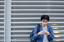 Giovane uomo in auricolare utilizzando smartphone all'aperto — Foto stock