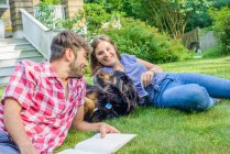 Casal na grama no jardim com cão, lendo — Fotografia de Stock