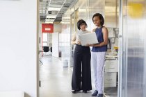 Two women standing in office corridor and looking at laptop — Stock Photo