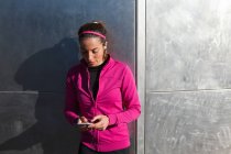 Jovem mulher em roupas esportivas mensagens de texto no smartphone — Fotografia de Stock
