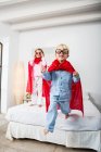 Мальчик и девочка-близнец в красных плащах прыгают с кровати — стоковое фото