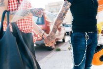 Пара татуированных хипстеров, держащихся за руки на тротуаре, посередине — стоковое фото