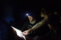 Три чоловіки дивляться на карту, вночі, використовуючи фари для світла — стокове фото
