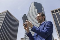 Businessman looking at digital tablet beside skyscrapers — Stock Photo
