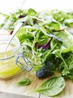 Green salad leaves and jar with sause on wooden desk — Stock Photo