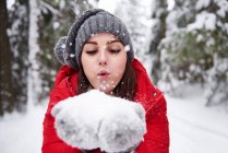 Joven mujer soplando copos de nieve de las manos - foto de stock