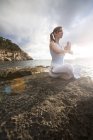 Женщина, сидящая на скалах по морю и медитирующая, Пальма де Майорка, Ислас Балеарес, Испания, Европа — стоковое фото