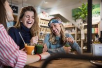 Three female friends, sitting in cafe, drinking smoothies, laughing — Stock Photo