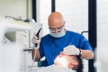 Dentista que realiza procedimiento dental en paciente masculino - foto de stock
