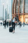 Mujer de negocios caminando con maleta de ruedas y teléfono inteligente - foto de stock