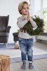 Young boy standing with hands together and holding wreath over arm — Stock Photo