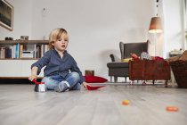 Молодий хлопчик сидить на підлозі з іграшковою пилою і пензлем — стокове фото