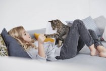 Девочка на диване играет с домашним котом — стоковое фото