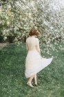 Femme en robe blanche tournoyant par arbre à fleurs — Photo de stock