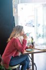 Женщина пьет кофе и держит смартфон в кафе — стоковое фото