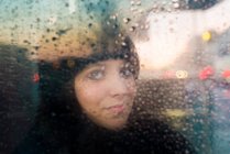 Femme regardant par la pluie fenêtre éclaboussée — Photo de stock
