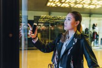 Женщина держит смартфон и смотрит в витрину магазина — стоковое фото