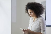 Junge Geschäftsfrau im Büro SMS auf dem Smartphone — Stockfoto