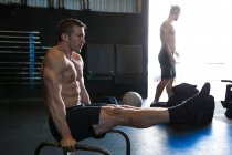 Homem exercitando-se no ginásio, usando barras paralelas, na posição L-sit — Fotografia de Stock