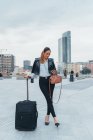 Портрет бізнес-леді, що тримає колісну валізу і використовує смартфон — стокове фото