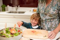 Мальчик помогает маме готовить салат вместе дома — стоковое фото