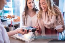 Female friends standing at counter in cafe, paying using credit card — Stock Photo