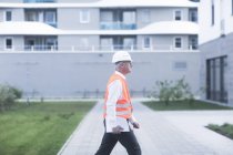 Visão lateral do trabalhador adulto da construção que caminha após o edifício — Fotografia de Stock