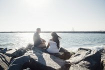 Couple sitting on coastal rocks, looking at view, rear view — Stock Photo