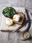 Still life with spinach and poached egg on toast on chopping board, overhead view — Stock Photo