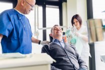 Чоловік пацієнт у стоматологічному кріслі, стоїть поруч з ним стоїть стоматолог — стокове фото