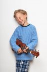 Menino tocando ukulele, olhos fechados, rindo — Fotografia de Stock