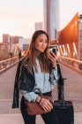 Молодая женщина с чемоданом на колесах с помощью смартфона — стоковое фото