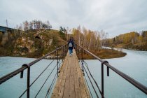 Rear view of small group of hikers walking over river footbridge, Kislokan, Evenk, Russia — Stock Photo