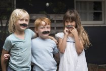 Crianças com bigodes falsos olhando para a câmera — Fotografia de Stock