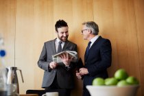 Two businessman chatting and reading newspaper in office boardroom — Stock Photo