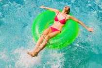 Mulher nova que flutua no anel inflável verde na piscina — Fotografia de Stock